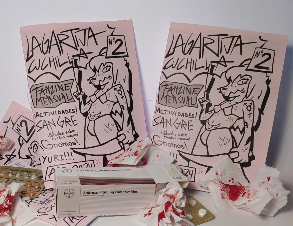 Fotografía de lanzamiento del segundo número. aparecen dos fanzines del segundo números y otro tirado en el fondo.
Hay una caja de Androcur 50 miligramos, varios surtidores de pastillas, y multiples papeles con sangre en el decorado. 