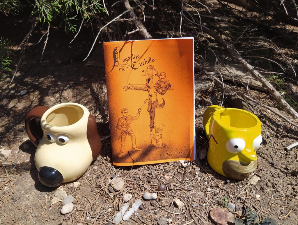 Fotografía de lanzamiento del decimoquinto número. en el se puede ver dos tazas, la de la izquierda es una taza con forma de Gromit y la de la derecha es una taza con forma de Homer Simpson. En el centro está el fanzine, de color naranja. Se puede apreciar que es un día soleado por las sombras duras de la imagen. el suelo es de tierra y al fondo se puede apreciar árboles.