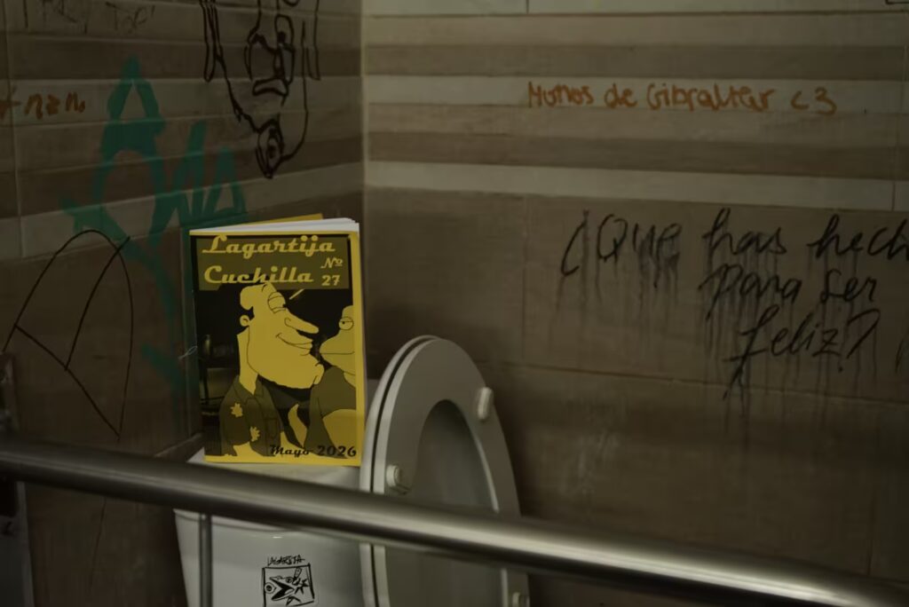 Fotografía del vigesimoséptimo número. El fanzine, de color amarillo, está en la izquierda encima de un retrete del cual tiene una pegatina de Lagartija Cuchilla. El baño esta lleno de grafitis en la pared de la izquierda, a la derecha hay solo dos textos en la pared: el primer texto es: "Monos de Gibraltar" y dibujaron un corazón. El segundo texto es: "¿Qué has hecho para ser feliz?"