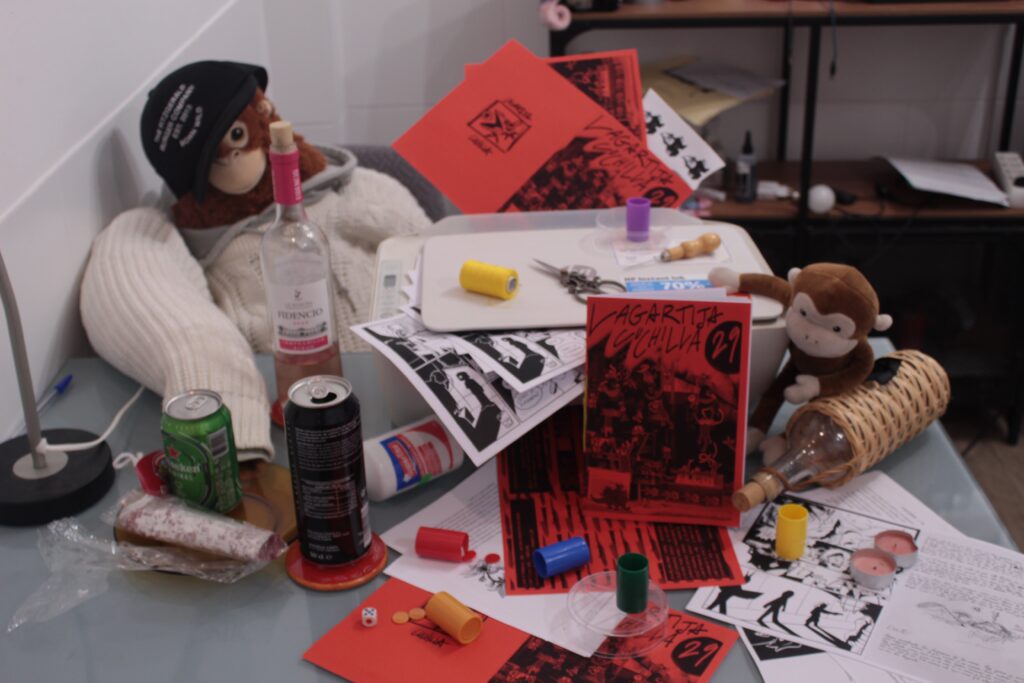 Foto del lanzamiento del número 29. 
Es una fotografía en la que se encuentra el peluche de mono gigante en representación a Juankinoto sentado con un licor y una gorra de la hamburguesería de Fitzgerald. a la derecha esta el fanzine de este mes, de color rojo oscuro, con varias latas y un peluche de mono pequeño, rodeado de numerosos fanzines sin montar y una impresora llena de fanzines de este mes montados de forma caótica.